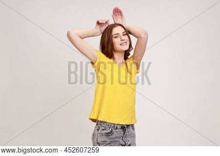 Portrait Of Funny Carefree Attractive Teenager Girl In Yellow T-shirt Showing Bunny Ears Gesture And