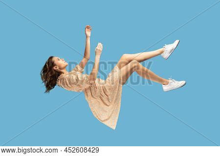 Floating In Air. Relaxed Girl In Yellow Dress Levitating, Looking Up While Flying Mid-air, Having Co