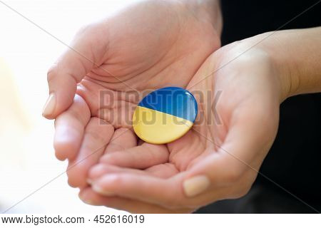 Female Hands Holding Badge With Flag Of Ukraine Closeup. Support Of Ukrainian People During War Conc