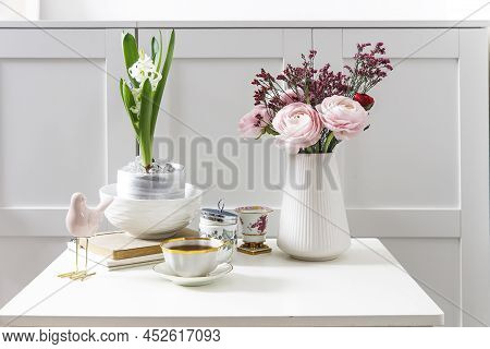 Bouquet Of Pink Persian Buttercups On A White Table In Front Of A Chest Of Drawers. Scandinavian Sty