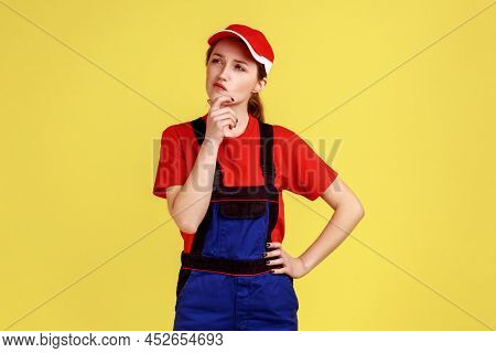 Portrait Of Pensive Handy Woman Standing And Holding Chin, Looking Away With Thoughtful Facial Expre