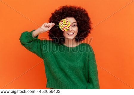 Playful Woman With Afro Hairstyle Wearing Green Casual Style Sweater Covering Mouth With Multicolor 