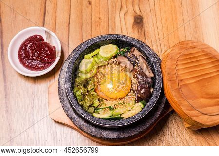 Bibimbap In A Black Heated Stone Bowl, Korean Traditional Dish- Bibimbap Mixed Rice With Vegetables 