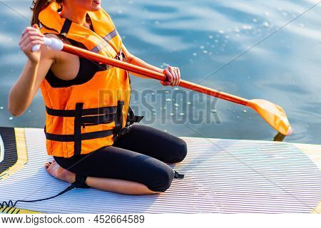 Young Woman In Orange Life Jacket On Supboard At River