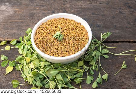 Fenugreek Seeds In A White Bowl With Raw And Organic Fenugreek Leaves Isolated On Wooden Background