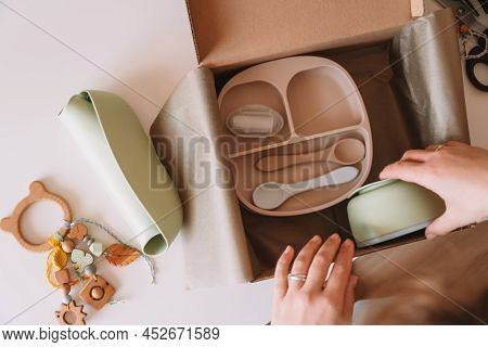 Cropped Woman Hands Packing And Wrapping Shipment With Silicone Baby Dish, Plate, Spoons, Bowl, Bib,