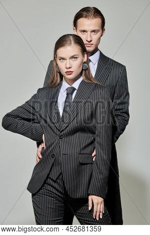 Fashion shoot. Portrait of stylish young man and woman in elegant striped pantsuits posing on a gray background. Impeccable look. Men's clothing style. 