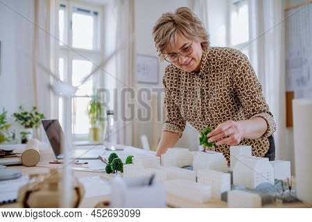 Senior Woman Eco Architect With Model Of Modern Bulidings Working In Office.