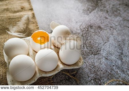 Fresh White Chicken Farm Eggs With Feathers In A Ceramic Box On A Brown Burlap Cloth Stand On A Gray