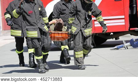 Four Firefightes And A Injured Person On The Stretcher On The Road After The Incident