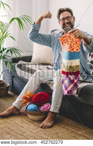 Enjoyed Adult Man Smile And Show His Knit Job Done With Colorful Wool Sitting On The Sofa At Home Du