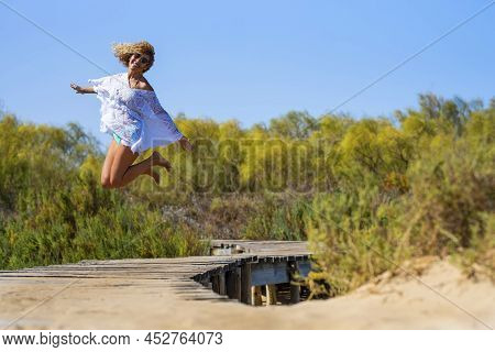 Carefree Woman Jumping Barefoot In Air On Elevated Footbridge Leading Towards Natural Forest. Crazy 