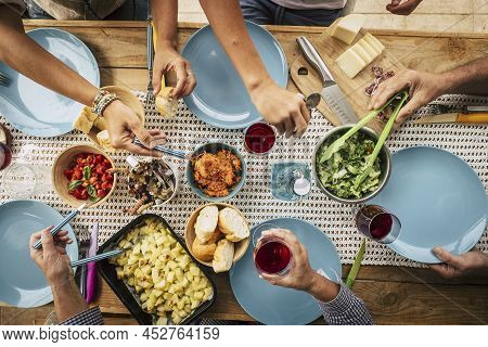 Group Of Friends Eating Together With Glass Of Wine On Dining Table. Hands Taking Food From Bowl On 