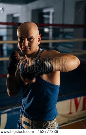 Vertical Shot Of Bald Aggressive Boxer Male Wearing Bandages Punching Air To Camera In Sport Club Wi