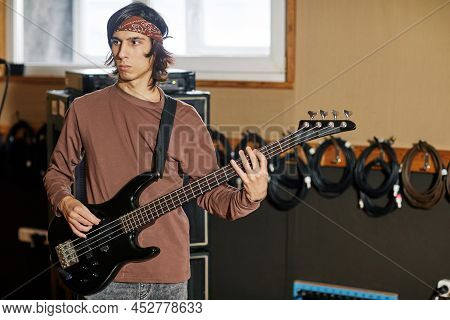 Waist Up Portrait Of Young Musician Playing Bass Guitar In Recording Studio, Making Rock Music, Copy