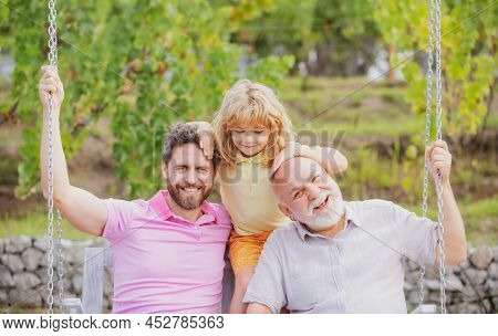 Grandfather With Son And Grandson On A Swing In Spring Garden Outdoors. Active Pring Leisure For Fam