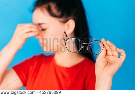 Close-up Portrait Of An Attractive Woman With Glasses In Her Hand On A Blue Background. The Poor You