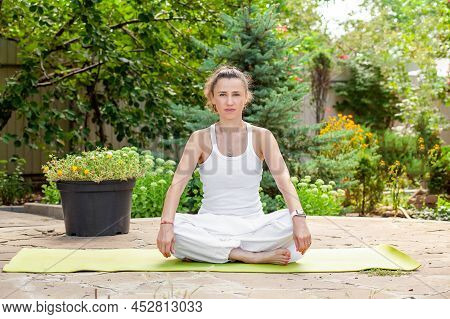 Young Woman Is Sitting In A Lotus Position Before Practicing Yoga, Looking Into The Camera.