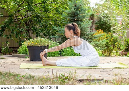 Young Woman Practices Yoga In The Courtyard Of A Country House. Paschimottanasana - Asana For Stretc
