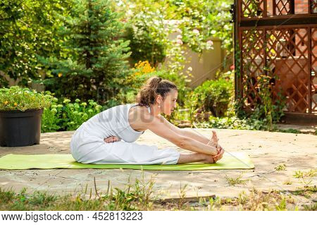 Young Woman Practices Yoga In The Garden. Ardha Padma Janushirshasana.
