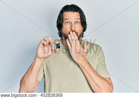 Middle age caucasian man holding sdxc card covering mouth with hand, shocked and afraid for mistake. surprised expression 