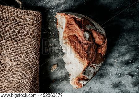 high angle view of a half round kamut wheat bread loaf on a mottled dark gray fabric surface, next to a burlap sack