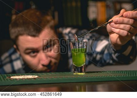 Bartender Taking Out Bar Spoon From Shot Glass With Green Drink