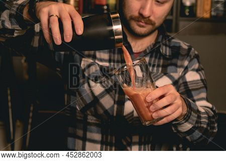 Bartender Pouring Cocktail From Shaker Into Tall Glass With Ice