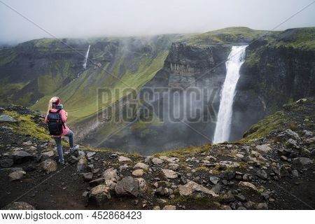 Woman With Backpack And Lilac Jacket Enjoying Haifoss Waterfall Of Iceland Highlands In Thjorsardalu