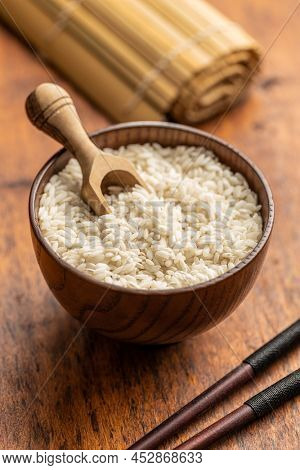 Uncooked Carnaroli risotto rice in bowl and wooden scoop on kitchen table.