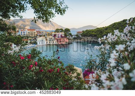 Assos Village On Kefalonia Island, Greece. Red And White Oleandre Flower Blossom In Foreground With 