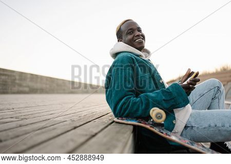 Cool Young African American Man With Skateboard Resting And Looking To The Side