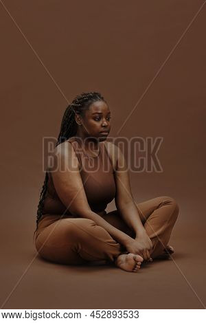 Portrait Of Young Black Woman In Casual Clothing Sitting With Blank Expression Isolated On Brown Bac