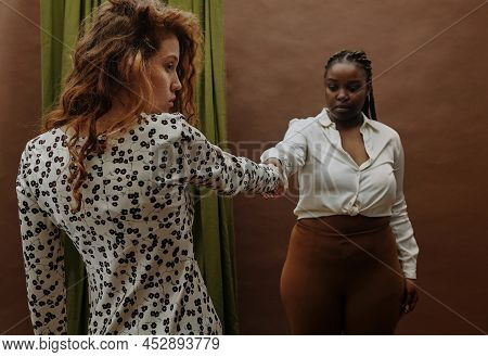 Young Black Woman Holding Hands With Her Girlfriend Standing Against The Brown Background