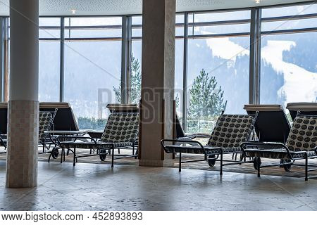 Empty Chaise Lounge Chairs Arranged In Lobby With View Of Snowy Mountains