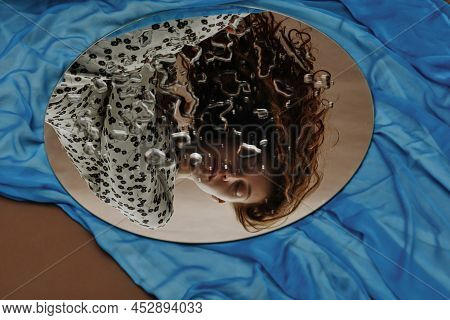 Young Ginger Woman Reflecting In Wet Mirror With Her Eyes Closed On Blue Background