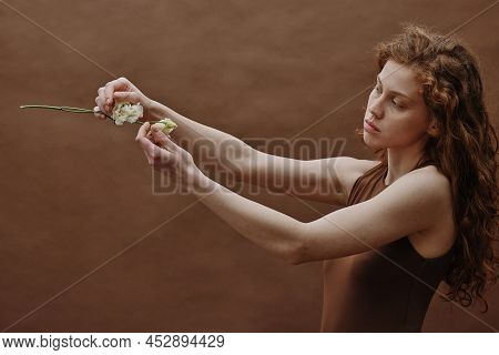 Young Red Headed Woman Holding White Flower In Front Of Her Face And Admiring Against The Brown Back