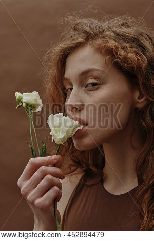 Portrait Of Ginger Young Girl Holding White Flower In Her Mouth Expressing Sensuality Isolated On Br