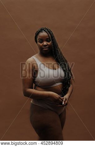 Portrait Of African Young Woman With Long Braids Having Plump Figure Standing In Underwear Against T