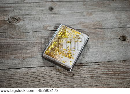 Pocket Mirror On A Wooden Background. Folding Rectangular Mirror With Floating Gold Sequins On A Gra