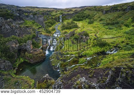 Gjain Watrfall Cascade, Colorful Lava Rocks Valley, Lush Green Moss And Vegetation And Blue Water St