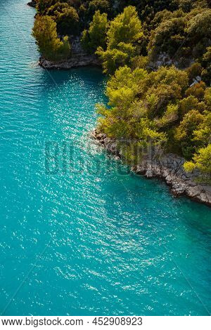 Azure Water Of The Lake And Slopes Of Mountains On A Background, Coast Line, Green Trees, Sun Light
