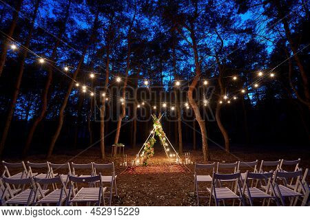 Festive String Lights Illumination On Boho Tipi Arch Decor On Outdoor Wedding Ceremony Venue In Pine