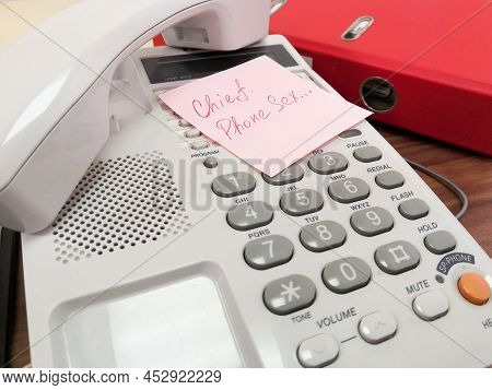 On The Keyboard Of The Landline Telephone Lies A Pink Square Leaflet With The Inscription In Red Ink