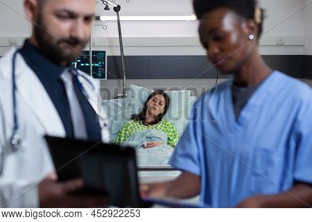 Patient On Hospital Bed Feeling Ill Waiting For Medic And Nurse To Read Diagnosis From Digtal Tablet