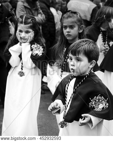 Elche, Spain- April 13, 2022: Children On Easter Parade With Bearers And Penitents Through The Stree