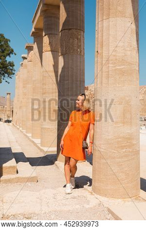 A Woman Stands In The Ancient Acropolis Of Lindos Against The Background Of The Colonade, Greece, Rh
