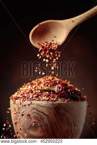 Chilli Flakes Are Poured Into A Wooden Dish. Chilli Flakes And Dried Chili Peppers On A Brown Backgr