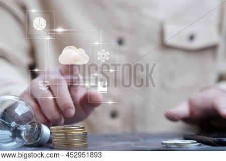 Person's Hand Next To A Stack Of Coins And A Lightbulb
