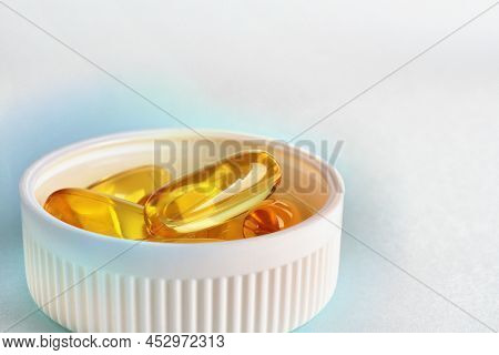 Yellow Softgels Or Capsules Are In White Bottle Cap. Fish Oil. Light Surface. Vitamins And Healthy L